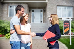 Realtor shaking hands with couple in front of their new home.