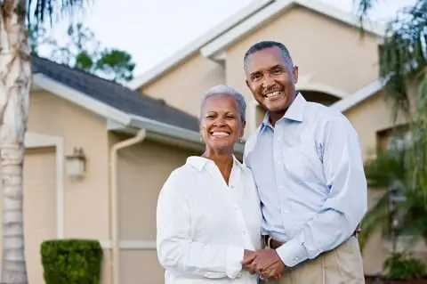 Older couple smiling in front of new home.